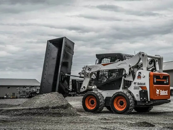  The image shows a Bobcat skid steer loader with a bucket attached to the front. The loader is parked on a dirt surface, and there is a pile of dirt in front of the bucket.
