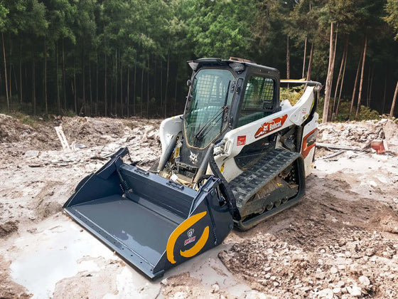 The image shows a bobcat skid steer with a bucket sitting in the mud. The bobcat is a yellow and black machine with the bobcat logo on the side. The bucket is also yellow and black, and it is tilted to the side. The background is a muddy field with some trees and bushes in the distance.