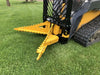 This is a yellow and black attachment mounted on the front of the skid steer. It has two large jaws made of steel, which are designed to grip and pull trees and stumps. The jaws are open in the image, and you can see the teeth on the inside that help to grip the wood.