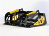 A yellow and black EZ-Grapple bucket attachment sitting on a gravel road. The EZ-Grapple is a skid steer attachment used for landscaping and construction work.