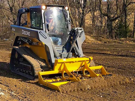 A skid steer loader with a land leveler attachment is used to level a dirt field.