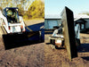 A skid steer with the black rectangular bucket sitting on top of a gravel road. 