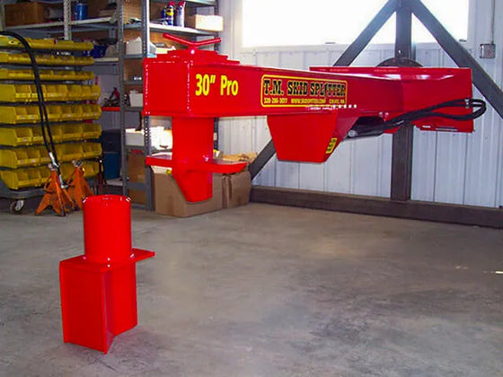 A red TM Manufacturing Pro 30 skid steer log splitter attachment parked in a garage.