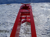 A TM Manufacturing Pro 30 skid steer log splitter attachment in the snow. The splitter is bright red and has a black metal frame with red hydraulic hoses and a control panel