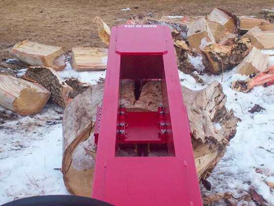 A red TM Pro skid steer log splitter sitting on top of a pile of logs in the snow. 