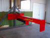 A red hydraulic log splitter sitting in a room with a window and a door. The splitter has a vertical beam attached to a horizontal beam, with a wedge on the end of the vertical beam. There is a control panel on the side of the machine.